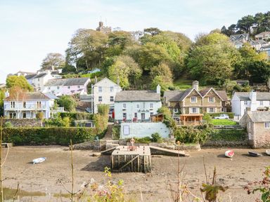 A riverside view of houses and a pier with boats on a low tide at Meadow Lodge in Newton Ferrers