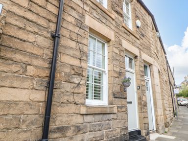 Stone exterior wall with two white doors and windows and a hanging basket on a street at Toll House in Corbridge