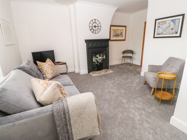 A living room with a grey sofa and cushions a black fireplace with flowers a grey armchair a small yellow table and a TV at Toll House in Corbridge