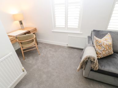 A small room with a wooden desk and chair a lamp on the desk a gray sofa with a cushion and a throw blanket at Toll House in Corbridge