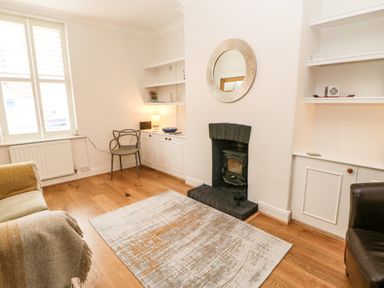 A living room with a fireplace a round mirror a rug wooden flooring and shelves at Toll House in Corbridge