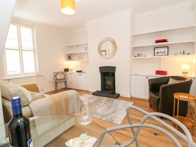 A living room with a fireplace a sofa a glass table with a wine bottle and glass and shelves on the walls at Toll House in Corbridge