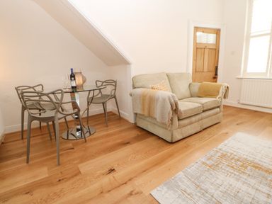 A living area with a glass dining table with four chairs a small sofa with throws wooden flooring and a door at Toll House in Corbridge