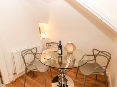 A dining area with a glass round table and four chairs with a bottle and wine glasses at Toll House in Corbridge