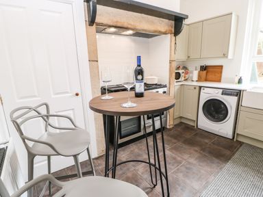 A kitchen with two gray chairs around a round wooden table with a bottle of wine and two wine glasses at Toll House in Corbridge