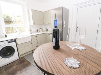 A kitchen with a wooden table holding a bottle of wine and two wine glasses near cabinets and a washing machine at Toll House in Corbridge