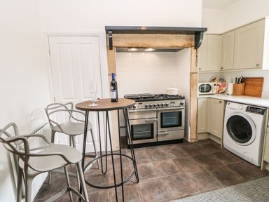 A kitchen with a stove under a stone hood a washing machine a microwave on a counter and a small table with two chairs at Toll House in Corbridge