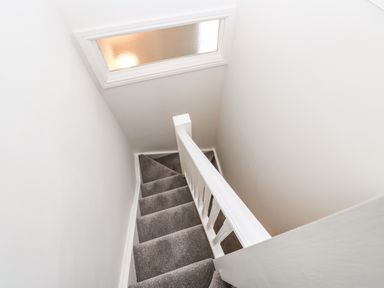 A narrow carpeted staircase with white walls and a frosted window at Toll House in Corbridge