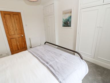 A bedroom with a bed covered with white and gray blankets wooden door radiator built in white wardrobes and a wall picture at Toll House in Corbridge