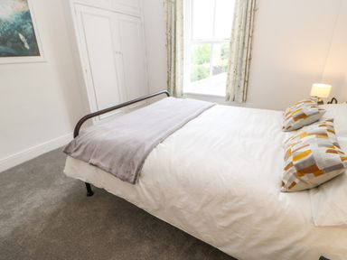 A bedroom with a bed with patterned pillows a gray blanket a window with curtains and a white built in wardrobe at Toll House in Corbridge