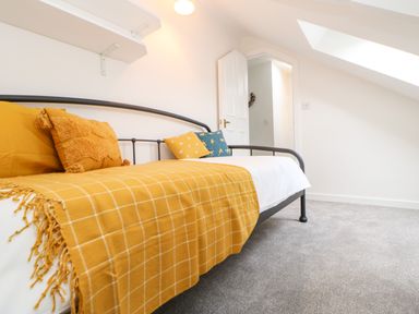 A bedroom with a black metal bed frame yellow blanket and cushions a white door and grey carpet at Toll House in Corbridge