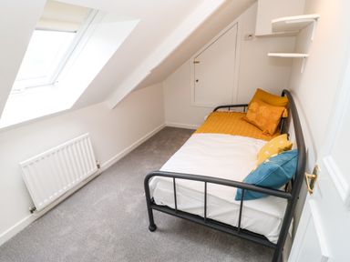 A small bedroom with a single black metal bed with cushions under a sloped ceiling at Toll House in Corbridge
