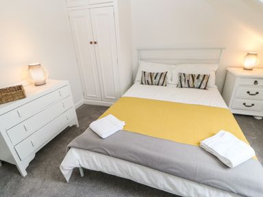 A bedroom with a double bed with yellow and gray bedding two dressers with lamps and folded towels at Toll House in Corbridge