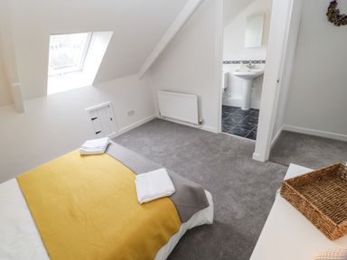 A bedroom with a bed covered with yellow and gray blankets and folded towels a skylight window and an open door leading to a bathroom with a sink and toilet at Toll House in Corbridge