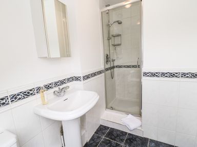 A bathroom with a pedestal sink a wall-mounted mirror a tiled shower enclosure and a folded towel on the floor at Toll House in Corbridge