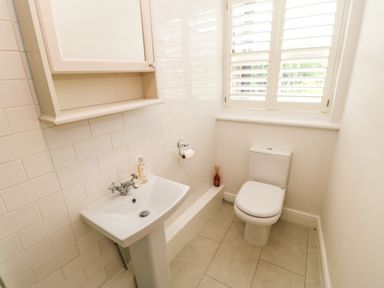 A small bathroom with a sink a toilet a cabinet and a window with shutters at Toll House in Corbridge