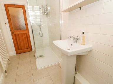 A bathroom with a shower enclosure a pedestal sink with soap and a wooden door at Toll House in Corbridge