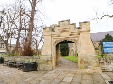 A stone archway entrance to a grassy path with benches and trees around at Toll House in Corbridge