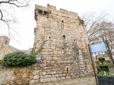 A stone medieval tower with narrow windows beside a church and a blue information sign at Corbridge