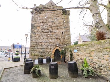 An outdoor space with a stone building and barrels arranged around plants at Toll House in Corbridge