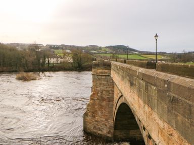 A stone bridge with street lamps over a river and fields in the background at Toll House in Corbridge