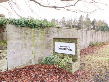 A stone welcome sign for Corbridge next to a stone wall with ivy and fallen leaves at Toll House in Corbridge