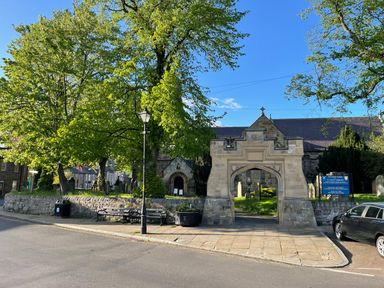 The entrance gate to a churchyard with benches trees and a car parked nearby at Toll House in Corbridge