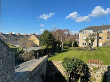 A garden with grass and trees next to stone buildings under a blue sky at Toll House in Corbridge