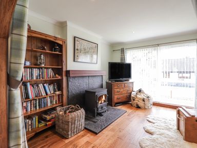 A living room with a bookshelf a wood stove a television on a wooden cabinet and a bean bag chair at The Hideout in Portree
