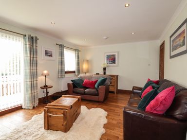 A living room with two brown leather sofas with cushions a wooden chest on a rug and curtains at The Hideout in Portree