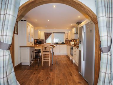 A kitchen with wooden floors white cabinets a silver refrigerator and a wooden archway at The Hideout in Portree