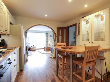A kitchen with wooden floor cabinets and a wooden table with chairs next to an archway leading to a living room at The Hideout in Portree