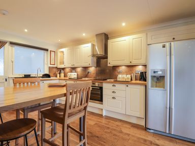 A kitchen with wooden table and chairs white cabinets and a double door refrigerator at The Hideout in Portree