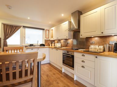 A kitchen with wooden chairs a table and white cabinets at The Hideout in Portree