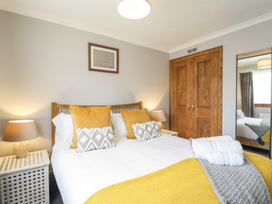 A bedroom with a bed white linens yellow and grey pillows bedside tables lamps a wooden wardrobe and a full length mirror at The Hideout in Portree