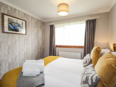 A bedroom with a bed with yellow and gray pillows towels on the bed and curtains on the window at The Hideout in Portree