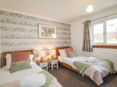 A bedroom with two single beds bedside tables and a window at The Hideout in Portree