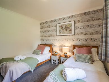 A bedroom with two single beds bedside tables lamps and a framed map on a floral wallpaper at The Hideout in Portree