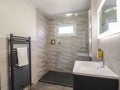 A bathroom with a walk-in shower a black towel rack and a sink with a mirror at The Hideout in Portree