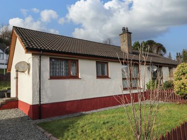 A single story house with white and red walls and a tiled roof with a small garden and bushes outside at The Hideout in Portree