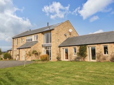 A stone farmhouse with multiple windows and doors surrounded by a lawn at Fontburn Farmhouse Ewesley near Rothbury