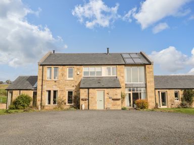 A stone farmhouse with multiple windows and a gravel driveway at Fontburn Farmhouse Ewesley near Rothbury