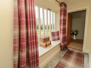 A hallway with a window seat and red plaid curtains and cushions and a matching rug at Fontburn Farmhouse in Ewesley near Rothbury