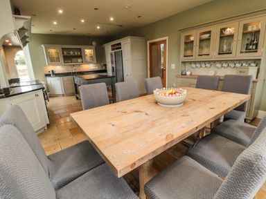 A kitchen with a wooden dining table and grey upholstered chairs at Fontburn Farmhouse in Ewesley near Rothbury