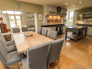 A kitchen and dining area with a wooden table and gray chairs at Fontburn Farmhouse in Ewesley near Rothbury