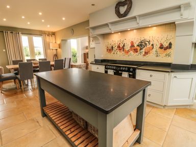 A kitchen with a central island and tiled backsplash with chickens next to a dining table with chairs at Fontburn Farmhouse Ewesley near Rothbury