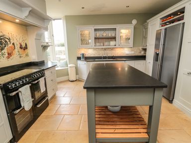 A kitchen with a central island a stove refrigerator cabinets and a window seat at Fontburn Farmhouse in Ewesley near Rothbury