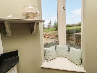 A windowsill seat with three cushions next to a window showing an outside garden at Fontburn Farmhouse in Ewesley near Rothbury