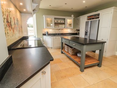 A kitchen with white cabinets a kitchen island with baskets on the lower shelf a refrigerator and stove at Fontburn Farmhouse in Ewesley near Rothbury