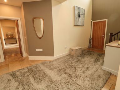 A hallway with a large rug a wooden door a mirror on the wall a basket and a painting at Fontburn Farmhouse in Ewesley near Rothbury